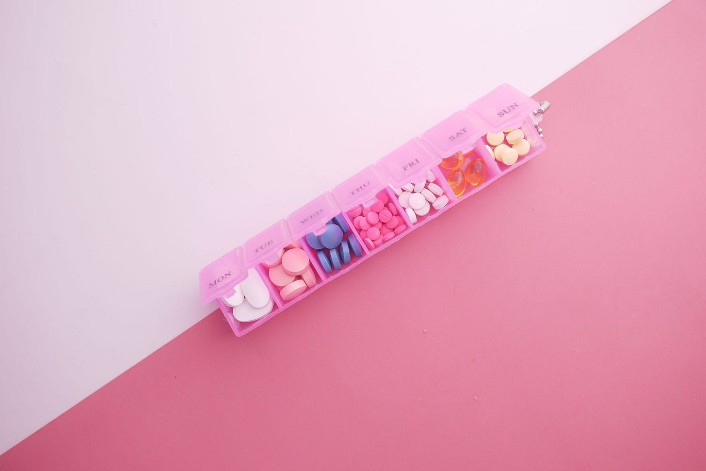 Photo by Towfiqu barbhuiya on Pexels A pink pill organizer with colorful tablets arranged for each day of the week on a vibrant pink background. (stock photo)