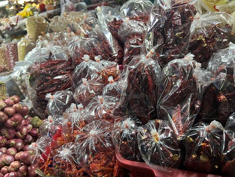 Outdoor farmers market in Chiang Mai with multicolored eggs, rows of produce, meats, and crickets.