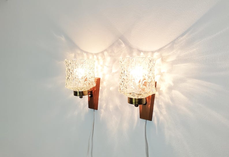 May include: Two wall-mounted light fixtures with clear glass shades and wooden bases. The shades have a textured pattern and the lights are turned on, casting a warm glow.