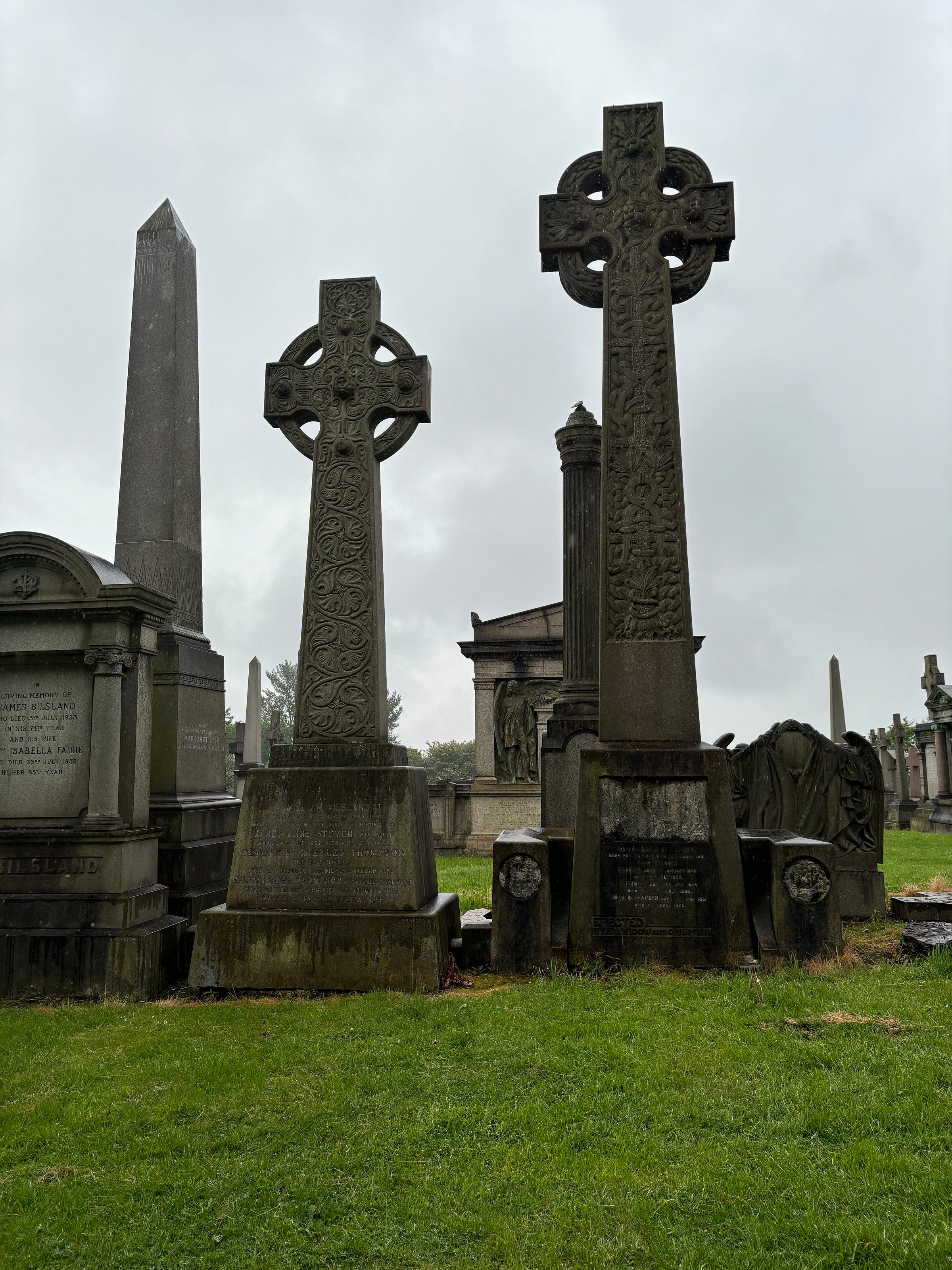 Two Celtic crosses, an obelisk and a few mausoleums on a rainy, overcast day in Glasgow.