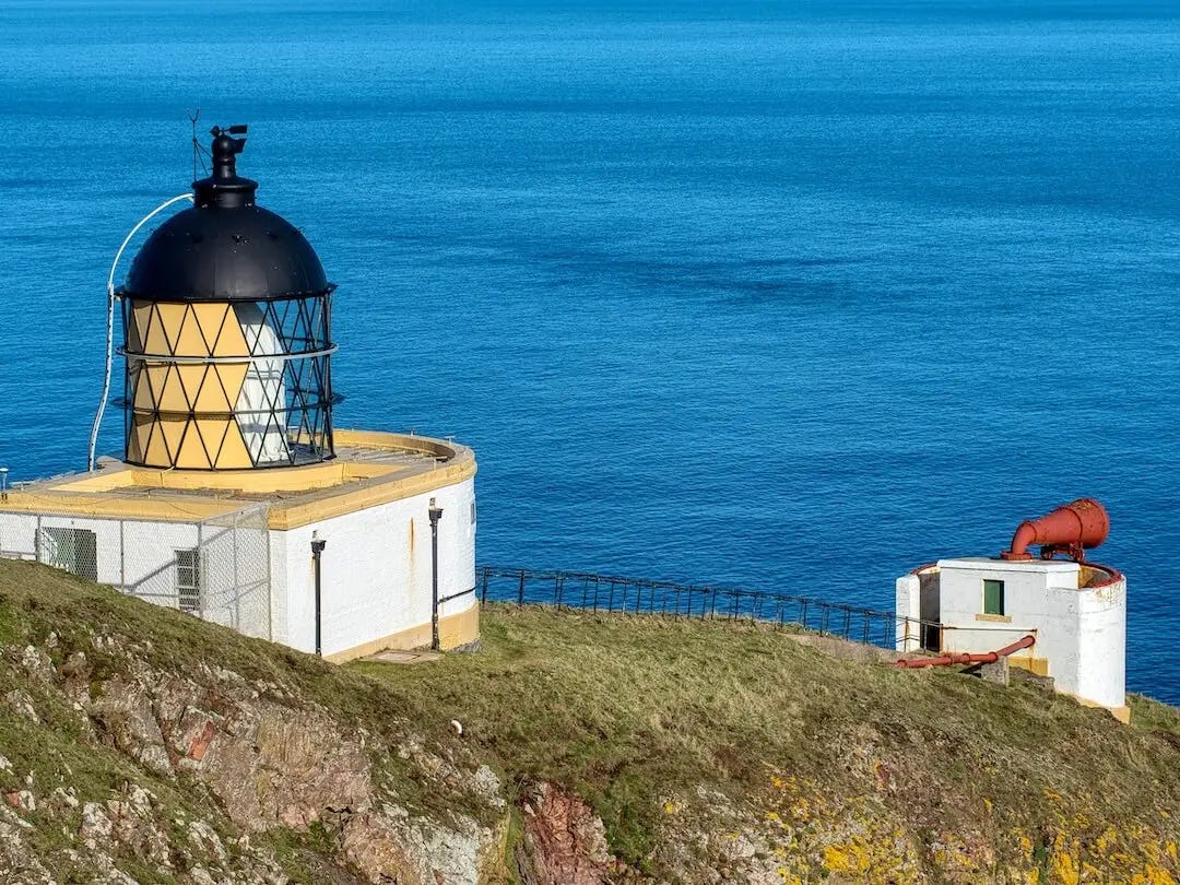 A short lighthouse built into the rock face with separate building for its horn