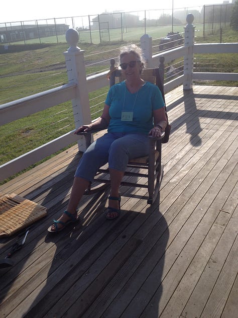 A rocker with a finished caned back, a group of caners show off their work, Jo in a blue t-shirt sitting in a finished rocker.