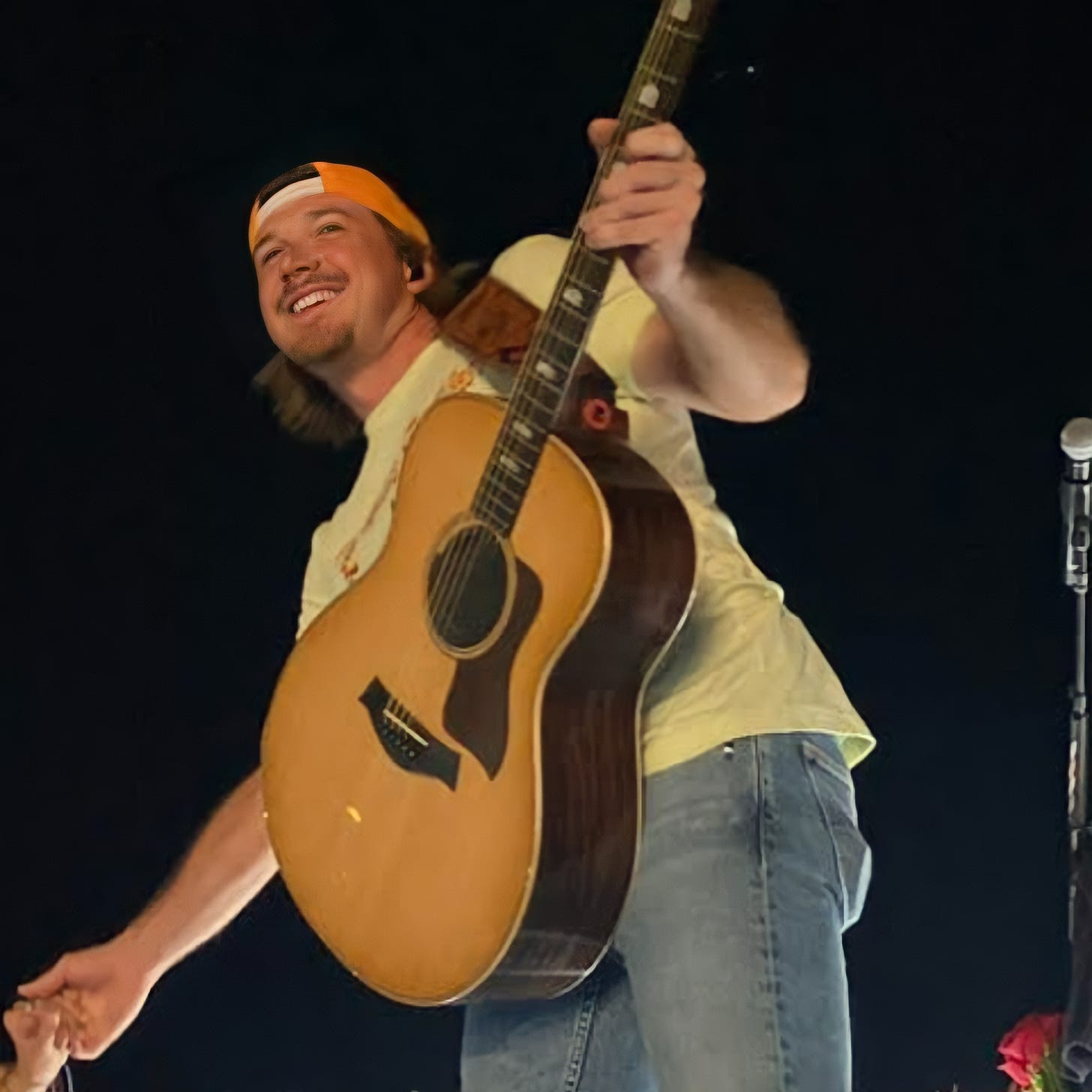Morgan Wallen smiles and holds a guitar during a 2022 performance