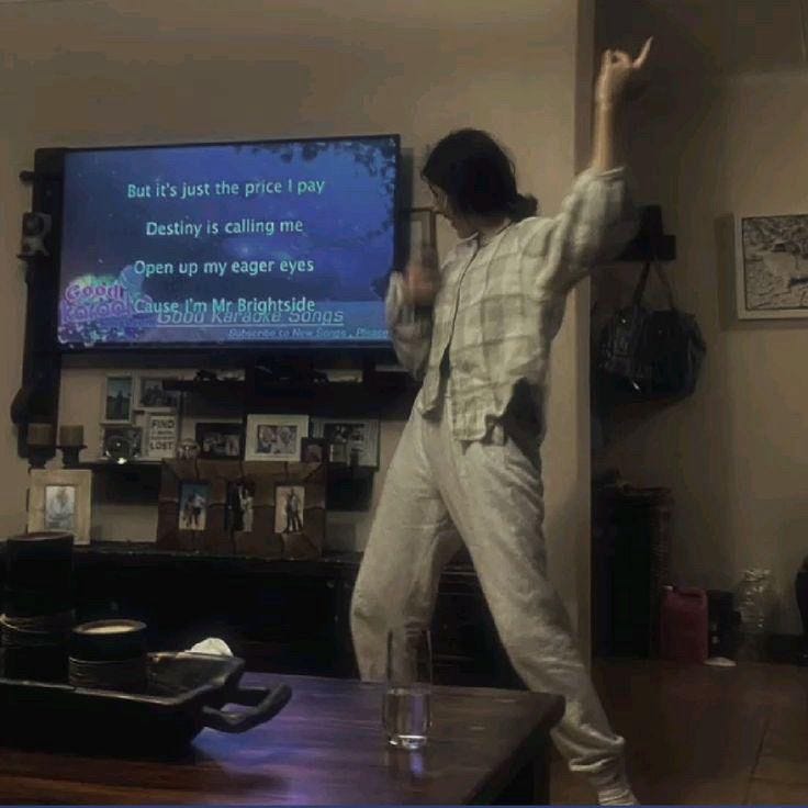 This may contain: a woman standing in front of a tv holding a remote control to play a video game