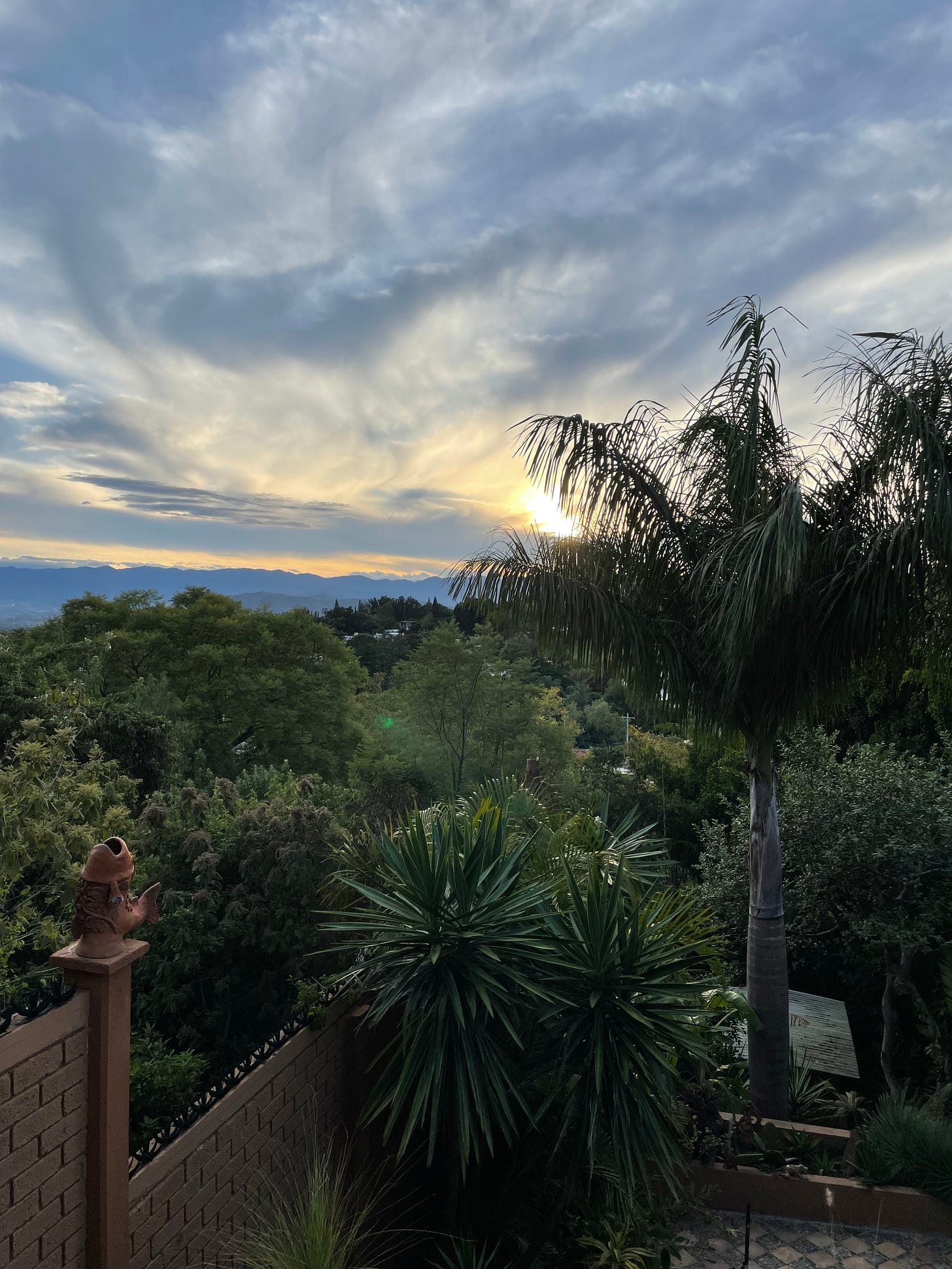 A view of a lush, green hill as the sun sets behind a layer of clouds.