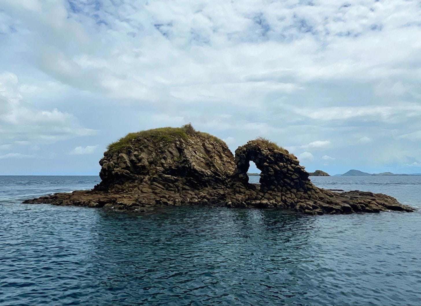 View of Batu Bolong rising from the sea in Komodo National Park, Indonesia, surrounded by deep blue waters. View of Batu Bolong rising from the sea in Komodo National Park, Indonesia, surrounded by deep blue waters.