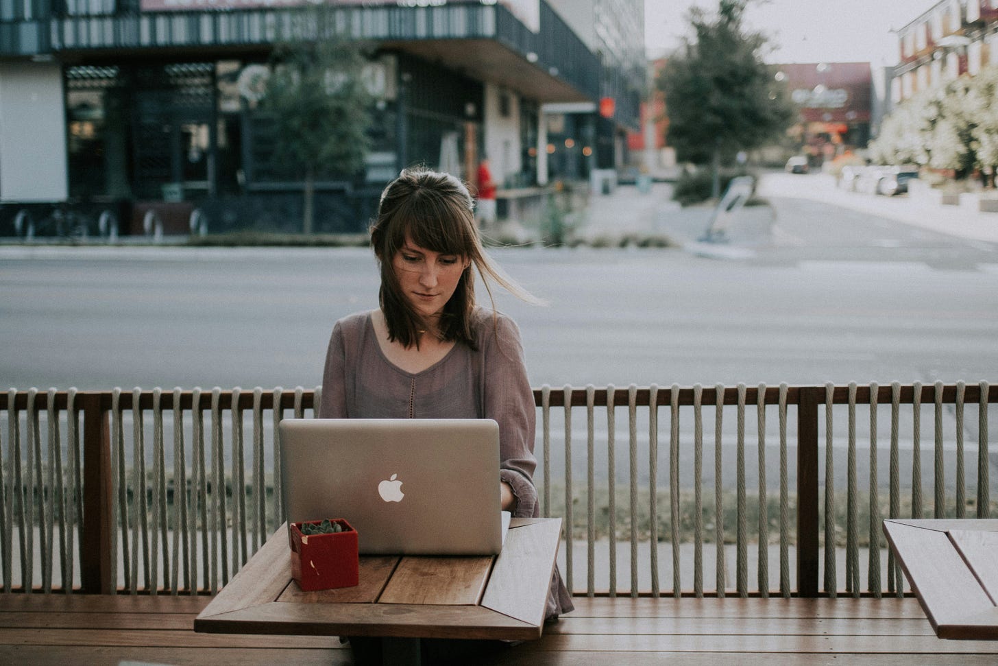 Woman working remotely sitting at a computer, outside a coffee shop in an upscale urban location