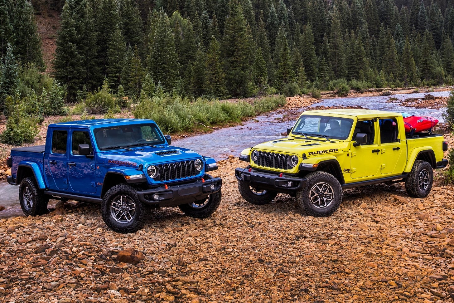 Two 2024 Jeep Gladiator models are parked on rocks near a mountain stream.
