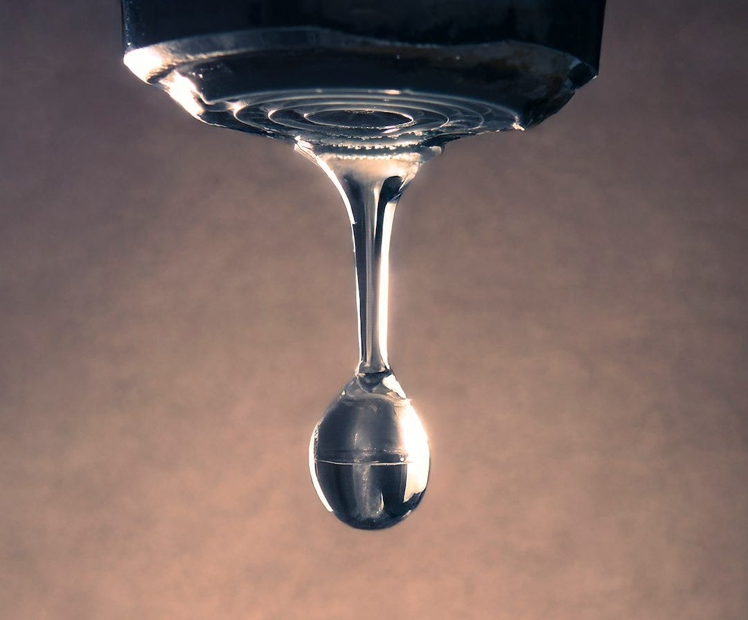 A water drop forms from a faucet. A water drop forms from a faucet.