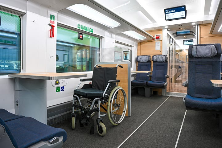 1. Image: White train from above, 2. Interior of the train, blue seats and wooden tables, 3. wheelchair space with an empty wheelchair and a wooden table 4. Accessible toilet with a lot of mirrors, a wide door and grabrails 