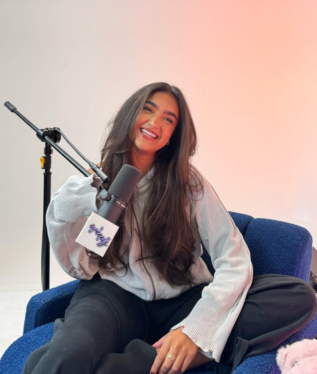 Miami-based creator Xime Ponch sitting in a professional podcast studio chair, equipped with a broadcast microphone and headphones. Capturing an 'unfiltered' conversation for The Beauty Ed® about her MAC Cosmetics collaboration and Gen Z beauty influence.
