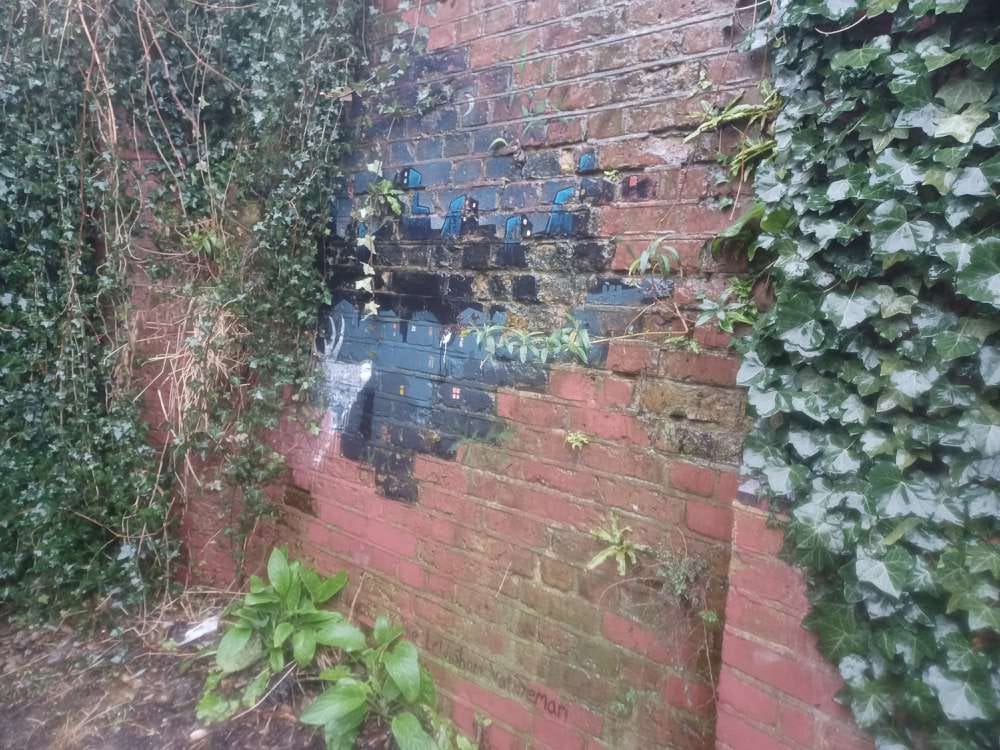 A mural featuing a white stag observing a night-time cityscape painted on a red brick wall surrounded by ivy A mural featuing a white stag observing a night-time cityscape painted on a red brick wall surrounded by ivy