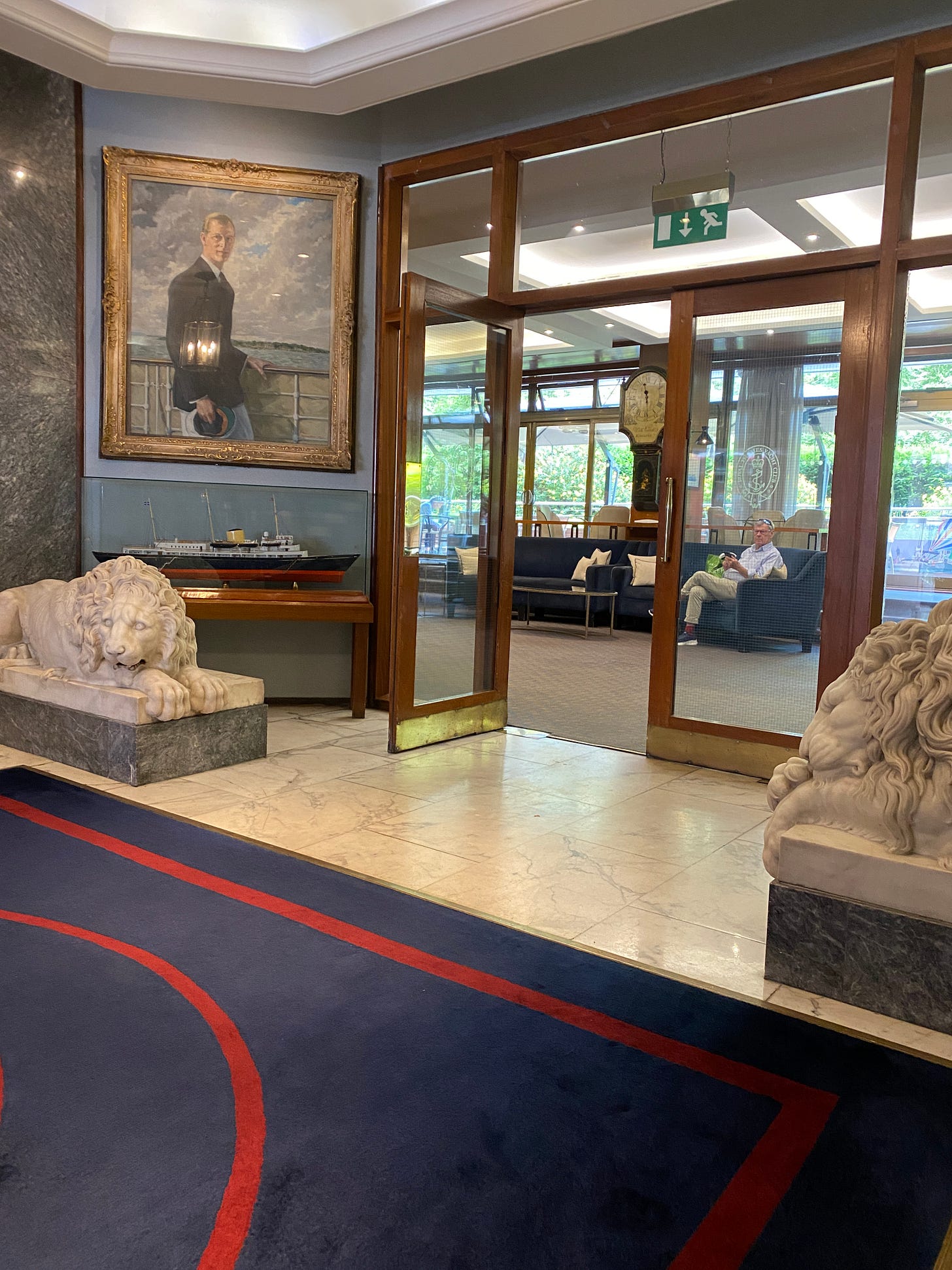 Elegant interior of Royal Thames Yacht Club showing marble floors, stone lion sculptures, formal naval portraits, and traditional British club furnishings