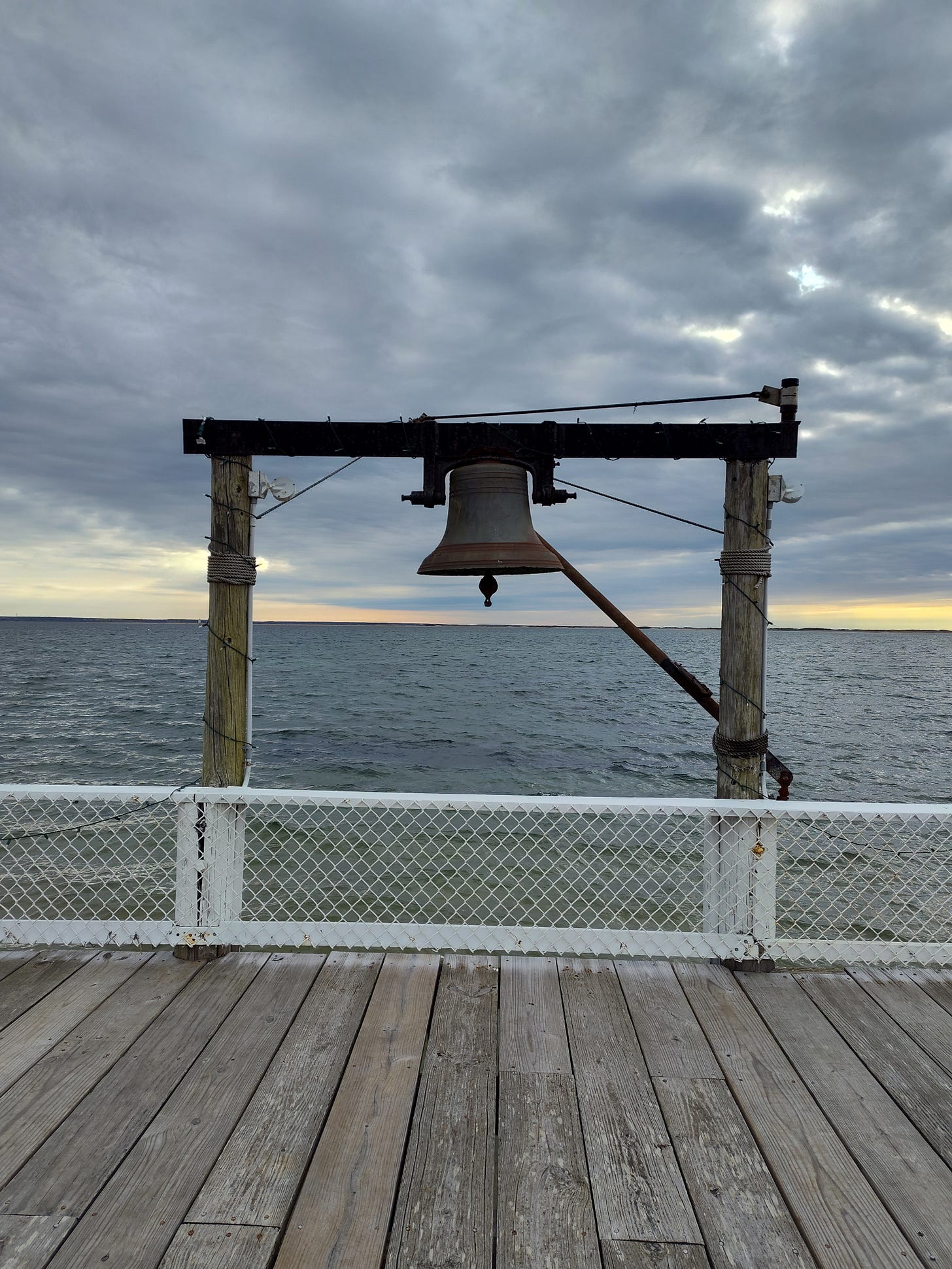 A bell at the end of a dock, moody sea and moody sky.