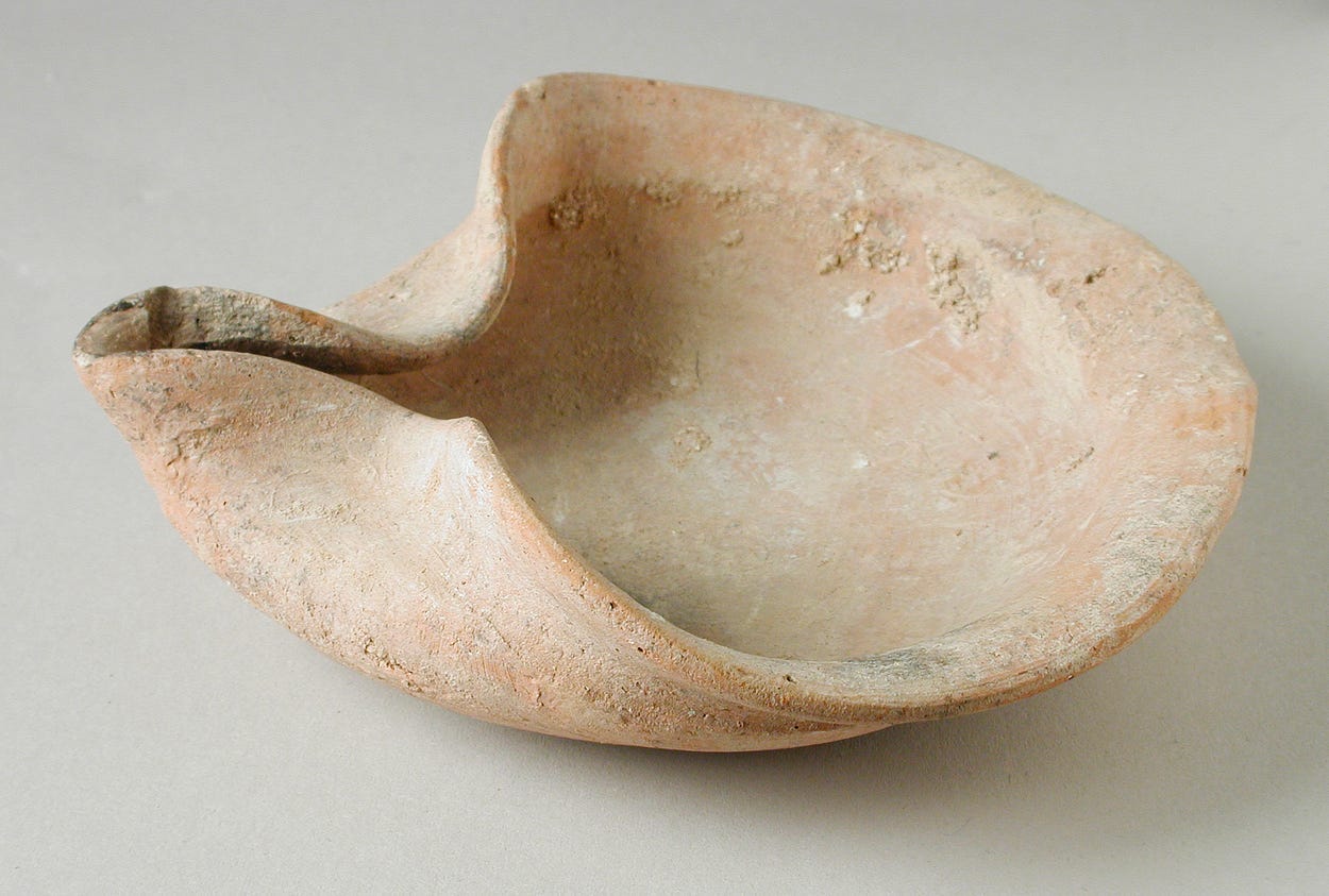 An ancient ceramic oil lamp, looking a bit like an oyster shell with the bottom end pinched together. An ancient ceramic oil lamp, looking a bit like an oyster shell with the bottom end pinched together.