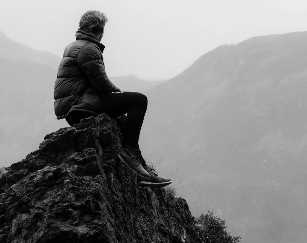 man in black jacket sitting on rock formation during daytime man in black jacket sitting on rock formation during daytime