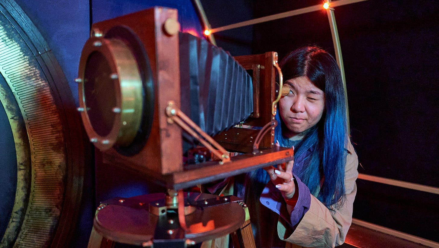 Someone peers through a "telescope" that looks like an old-school camera