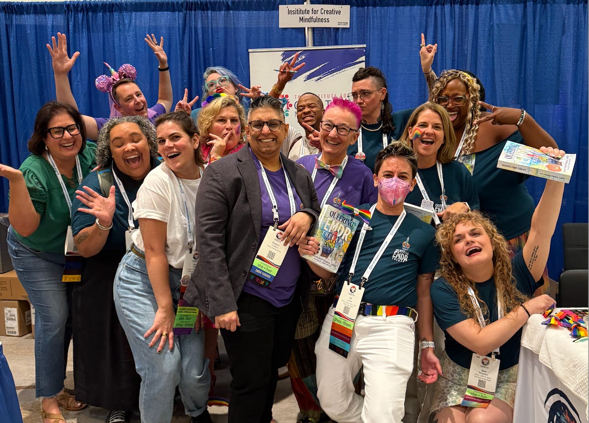 A group of 14 individuals of various backgrounds pose in a celbratory way around the book Queering EMDR Therapy