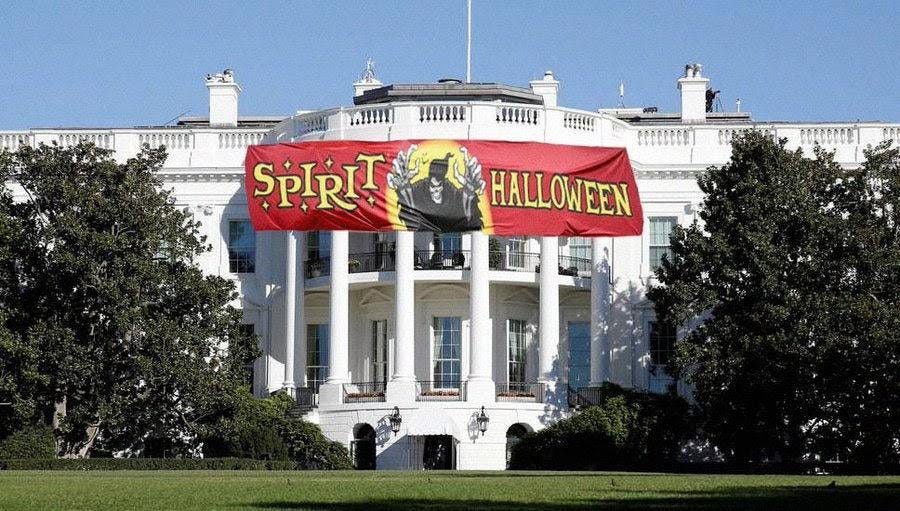 A large red banner with yellow text reading "Spirit Halloween" and an image of a witch, displayed across the front of the White House. The building is white with columns and surrounded by green lawns and trees.