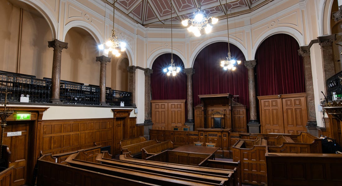 A courtroom with white walls, hanging chandeliers, and wooden benches A courtroom with white walls, hanging chandeliers, and wooden benches