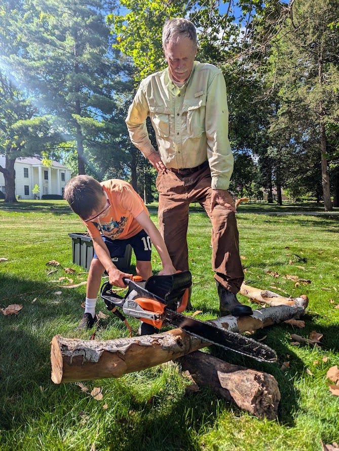 My dad, Harlan, supervises his grandson in learning the chainsaw.