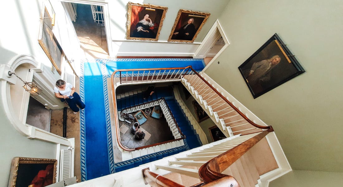 A spiral staircase with a blue carpet and green walls with paintings on them A spiral staircase with a blue carpet and green walls with paintings on them