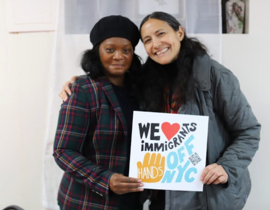 two women smiling and holding a sign that says "We heart immigrants. Hands off NYC" with a hand on it two women smiling and holding a sign that says "We heart immigrants. Hands off NYC" with a hand on it