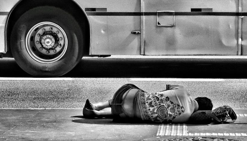 grayscale photography of person laying on ground near bus