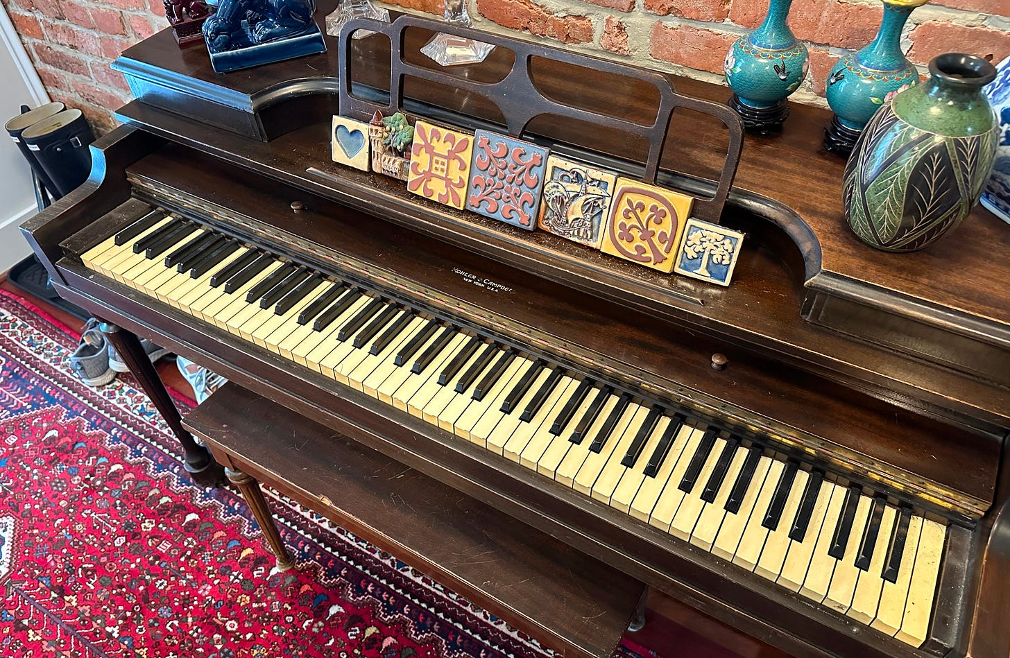 Antique upright piano in a living area on top of a red oriental rug. Antique upright piano in a living area on top of a red oriental rug.