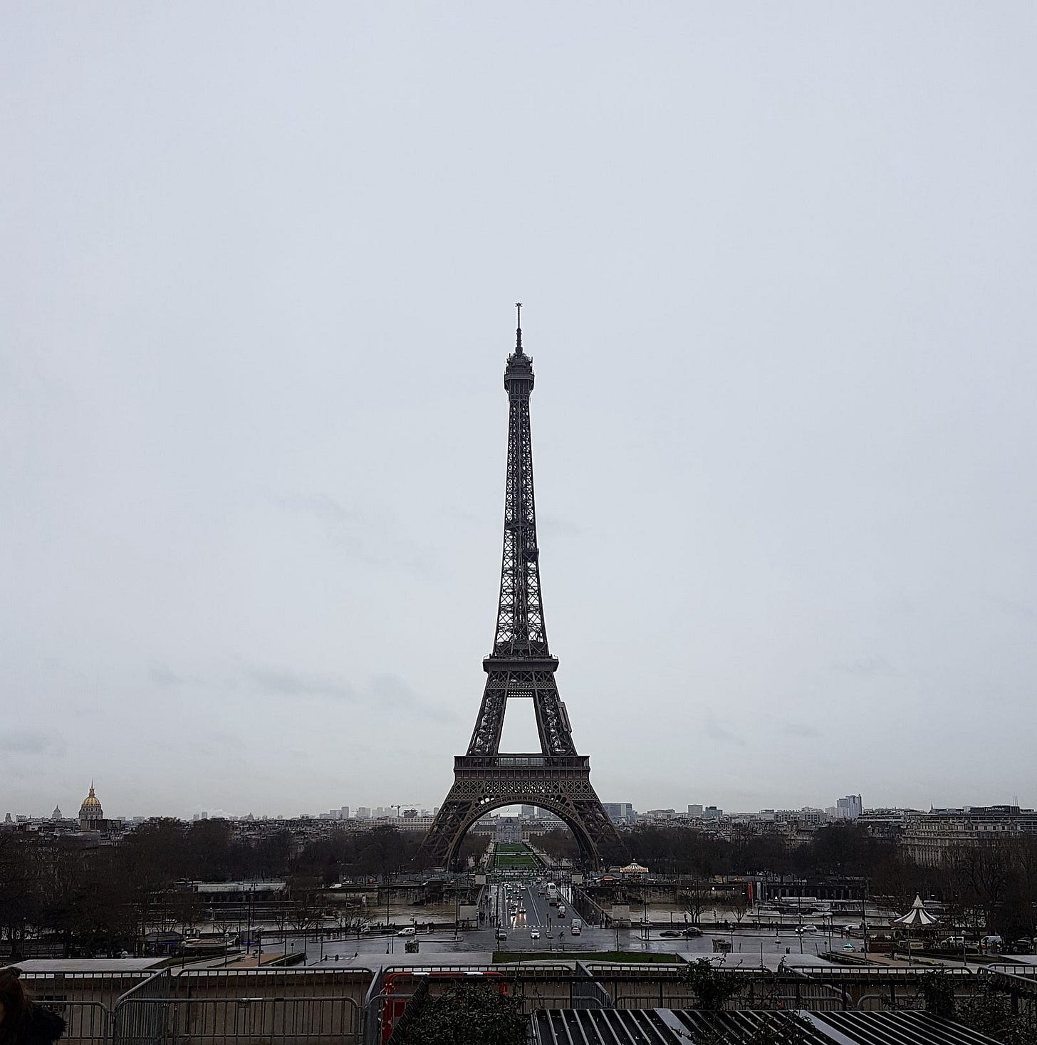 A photo of the Eiffel tower from a distance, set against a dim grey overcast sky.