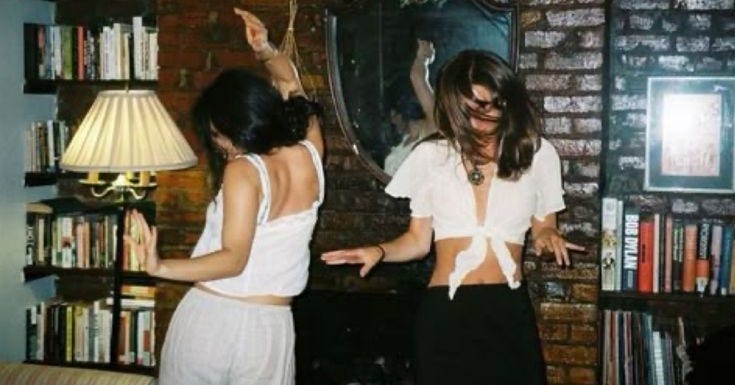 This may contain: two women standing in front of a brick wall with books on the shelves behind them This may contain: two women standing in front of a brick wall with books on the shelves behind them
