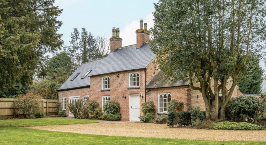 A brick house with a slate roof and white door with a path in front of it and trees around it A brick house with a slate roof and white door with a path in front of it and trees around it
