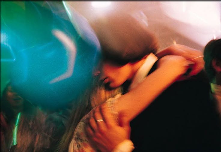 This may contain: two people hugging each other in front of a blue ball on the floor at a party