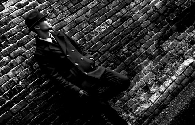 man wearing black coat leaning on brown brick wall