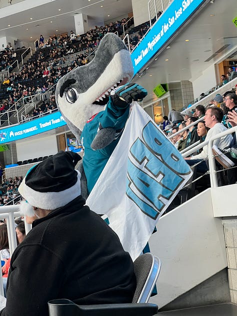 images of hockey arena, 2 girls wearing masks, a mascot shark on ice