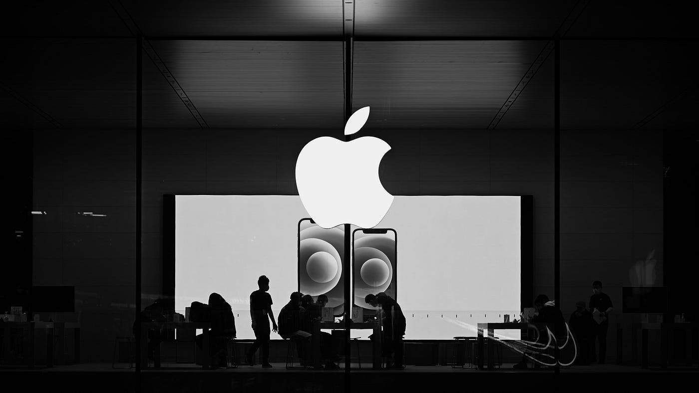 Black-and-white photo of people working inside an Apple Store under the glowing Apple logo, showcasing minimalist design and brand coherence. Black-and-white photo of people working inside an Apple Store under the glowing Apple logo, showcasing minimalist design and brand coherence.
