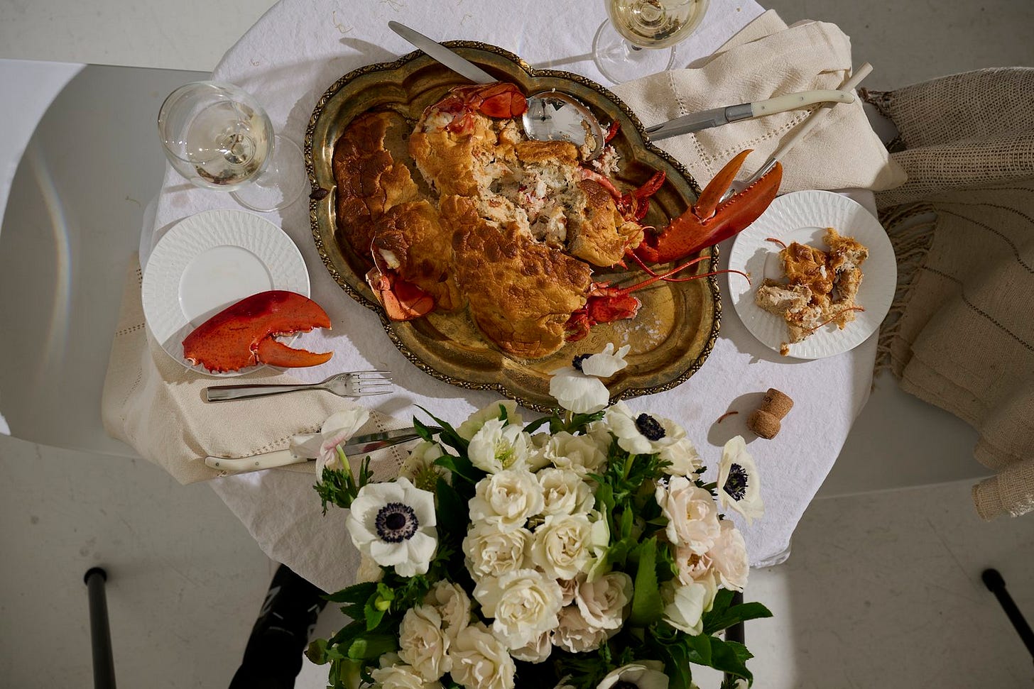 Lobster soufflé served on a vintage silver tray, partially carved, with lobster claws on display and white wine, crystal glassware, and floral centerpiece on a romantic table setting.