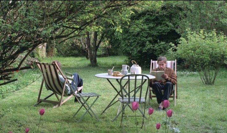 This may contain: two people sitting at a table outside in the grass with pink tulips around them