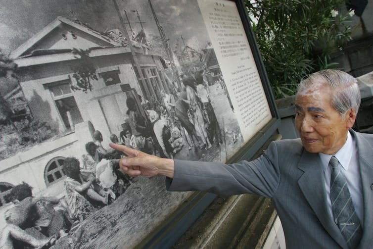 An old Japanese man in a grey suit who is a survivor of the Hiroshima bombing pointing to himself in photograph taken three hourse after the bombing. An old Japanese man in a grey suit who is a survivor of the Hiroshima bombing pointing to himself in photograph taken three hourse after the bombing.