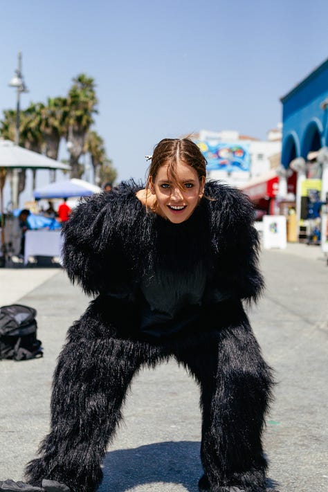 Barbara Palvin and Ashley Hart on set, laughing and posing with a gorilla suit—pulling it on, peeling it off, and mixing fashion with absurdity during the Mambo Goddess campaign shoot.