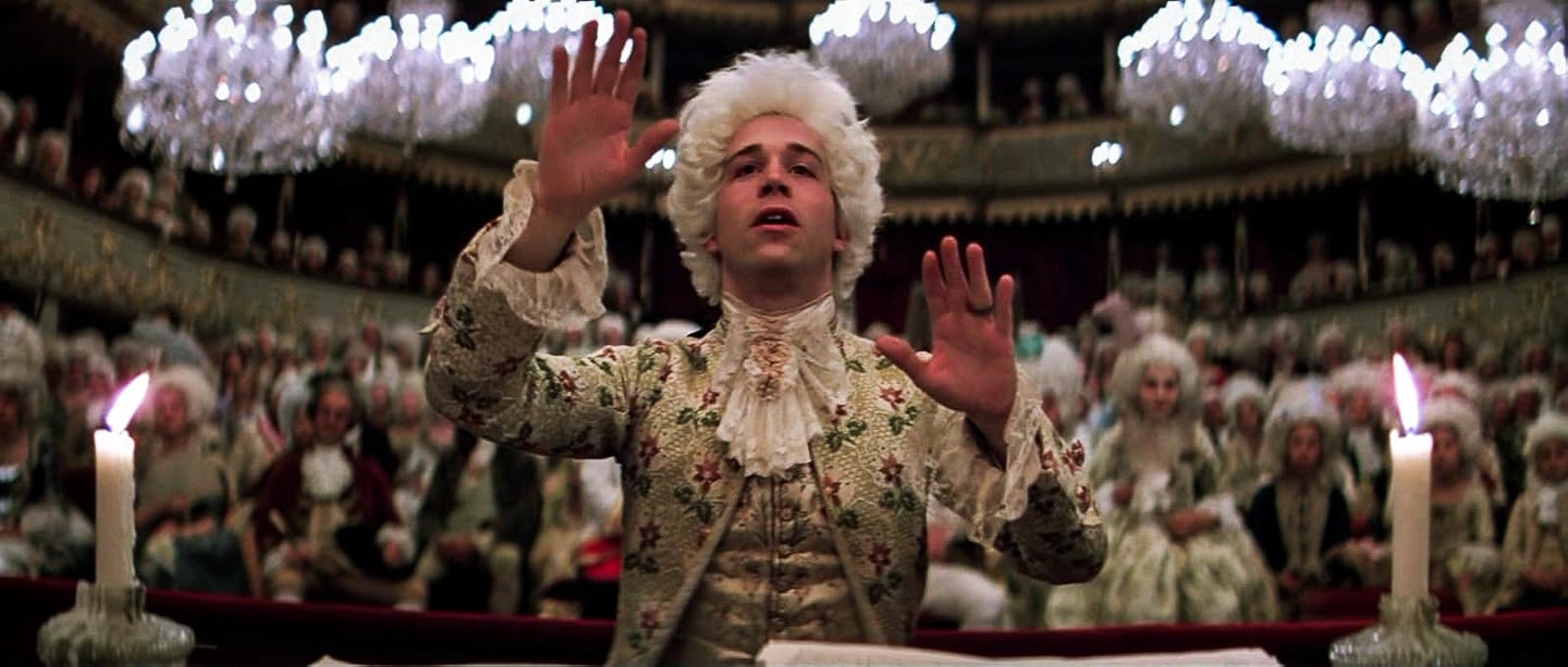 Tom Hulce as Mozart, arms raised mid-conduct in Amadeus, framed by glowing chandeliers and costumed onlookers in a lavish 18th-century opera house. Tom Hulce as Mozart, arms raised mid-conduct in Amadeus, framed by glowing chandeliers and costumed onlookers in a lavish 18th-century opera house.