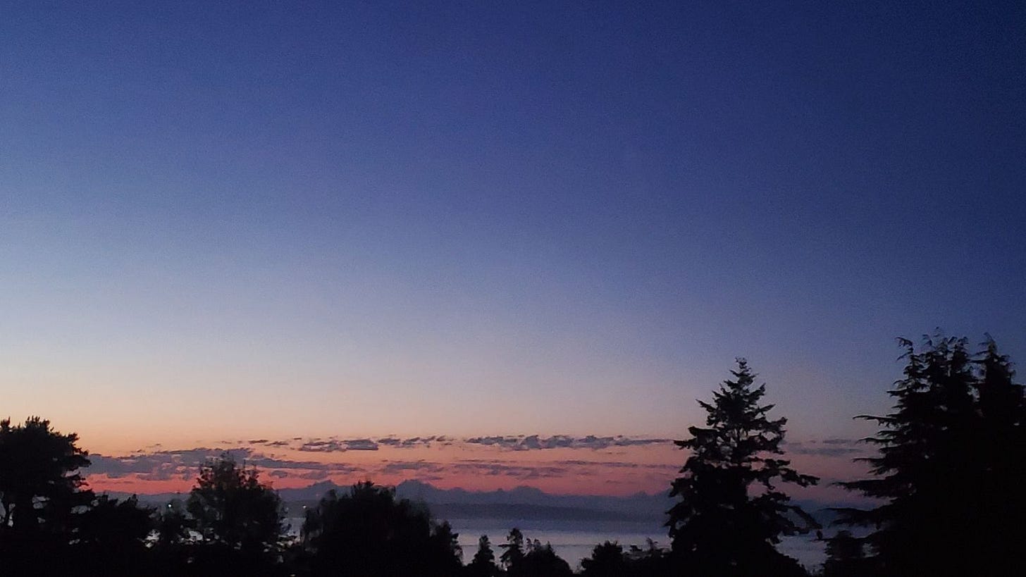 June 21, 2024: Early summer dawn viewed from the rear of the Adams Pragge House across Uptown Port Townsend toward Admiralty Inlet, with the Cascade Mountains visible beyond..