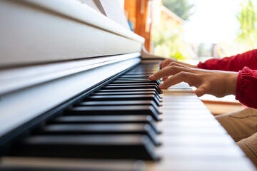 Cropped anonymous child playing piano while reading notes and rehearsing song at home