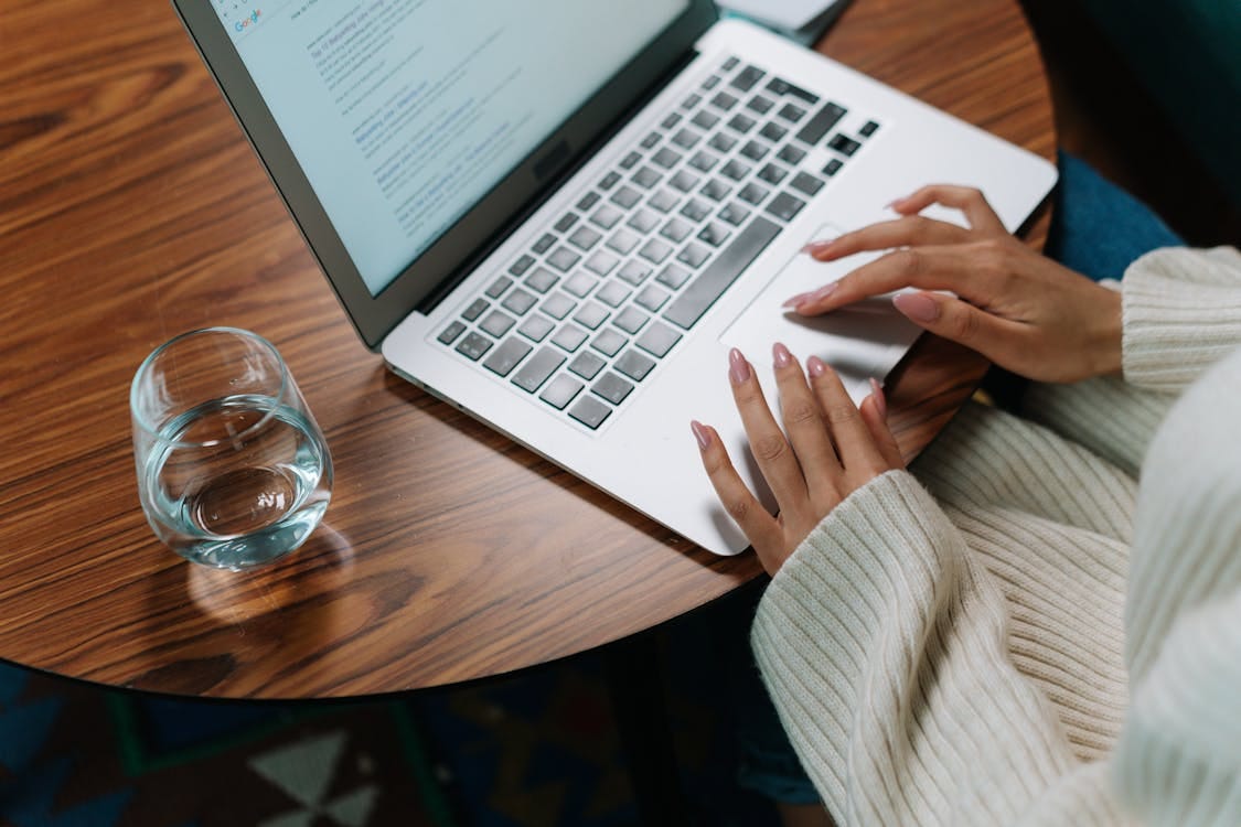 Free A person working on a laptop at a wooden table with a glass of water. Stock Photo