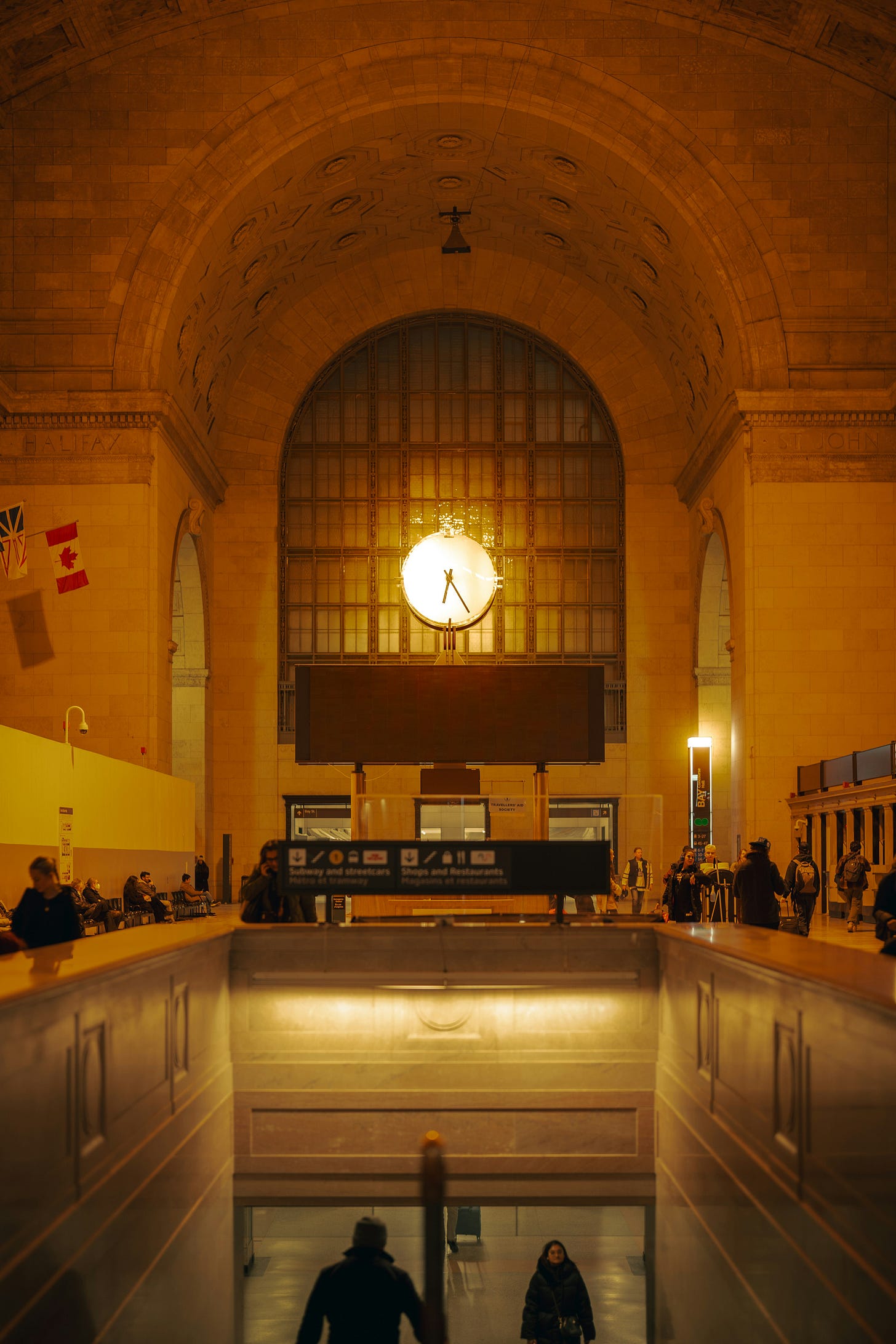 Main hall inside of train station with a couple of people walking up and down the stairs.