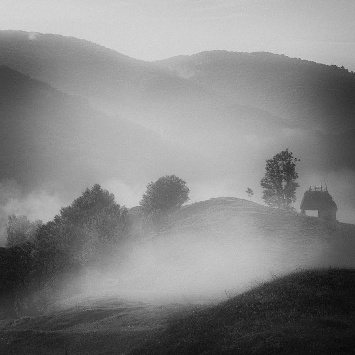 A selection of four images from Romania in black and white, one shows the rural landscape shrouded in mist, the second shows a haystack on a hillside and the other two show a blacksmith and an old man with a magnificent beard 
