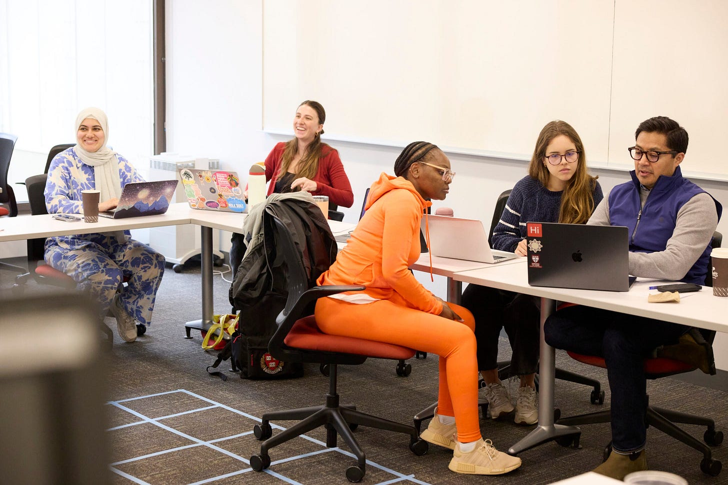 Students sit at tables working in groups in a classroom.