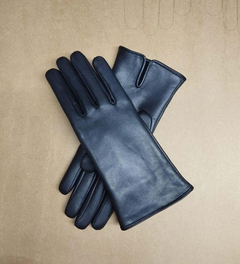 May include: A pair of black leather gloves with a fingerless design. The gloves are folded in half and laid flat on a brown surface.