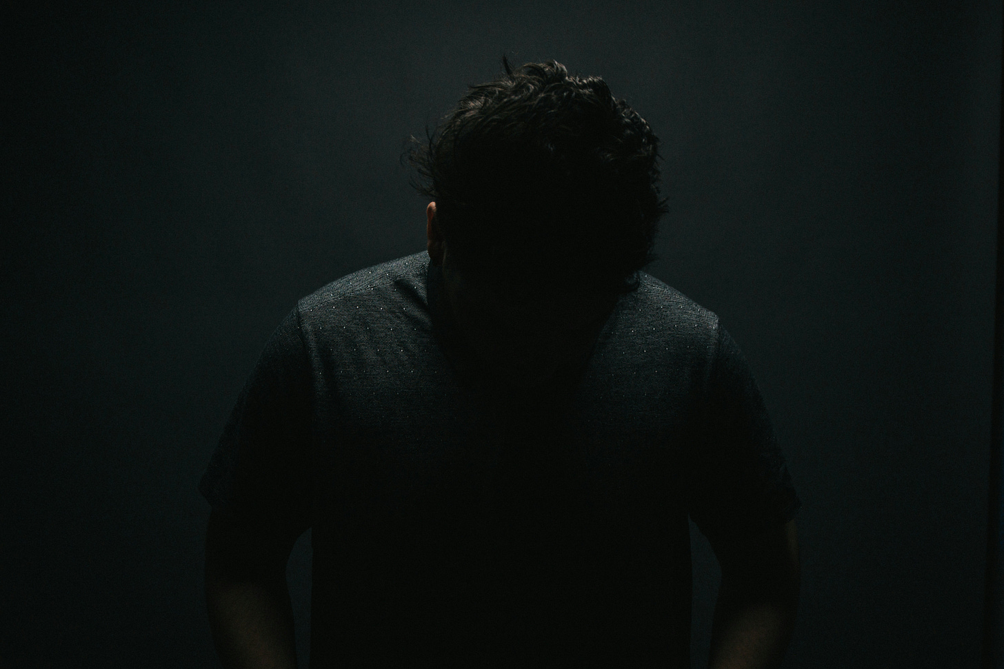 A greyed out image of a man with his head down in the shadows A greyed out image of a man with his head down in the shadows