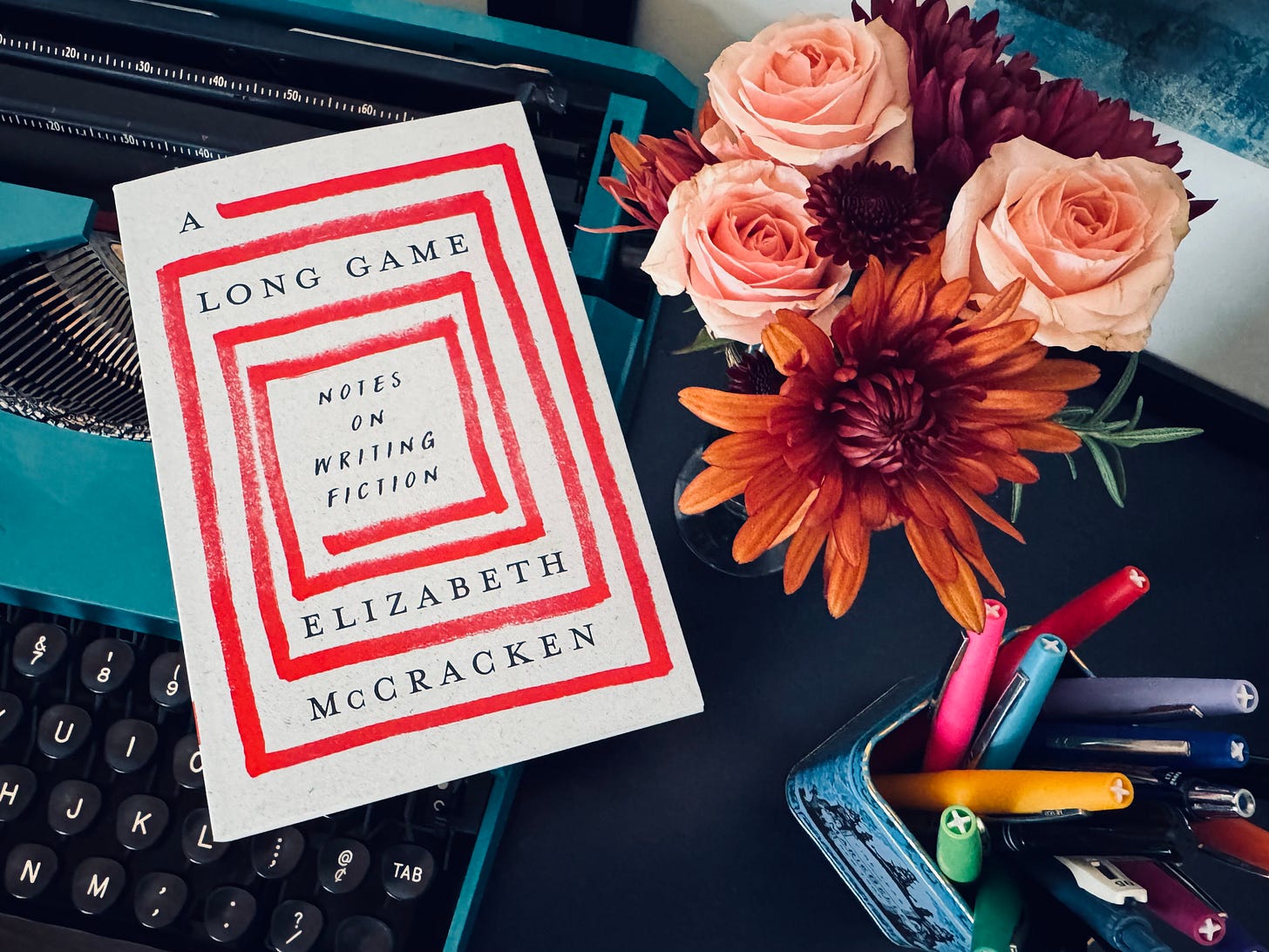 A photo of a typewriter, some flowers, and Elizabeth's book, A Long Game